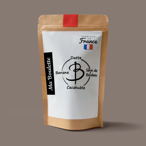 Une photographie commerciale du produit energy balls Banane-Cacahuète-Bouleau sur un fond marron gris. Le produit est contenu dans un sachet craft avec une étiquette contenant l'inscription "Fabriqué en France"