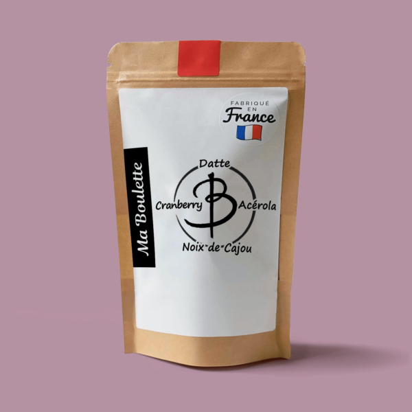 Une photographie commerciale du produit energy balls Cranberry-Cajou-Acérola sur un fond rose. Le produit est contenu dans un sachet craft avec une étiquette contenant l'inscription "Fabriqué en France"