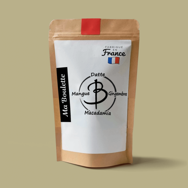 Une photographie commerciale du produit energy balls Mangue-Macadamia-Gingembre sur un fond beige. Le produit est contenu dans un sachet craft avec une étiquette contenant l'inscription "Fabriqué en France"