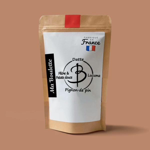 Une photographie commerciale du produit energy balls Pêche & Patate douce-Pignon de pin-Lucuma sur un fond orange. Le produit est contenu dans un sachet craft avec une étiquette contenant l'inscription "Fabriqué en France"